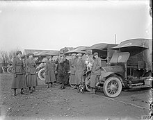Eight women in military uniform stand in front of vehicles in a black and white photo