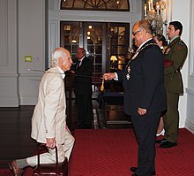 James McNeish kneeling in front of Sir Anand Satyanand as he is investiture