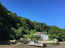 A building with a dock area for boats, surrounding by trees and dried-up river bed