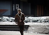 Braving snipers, a man runs out from the cover of a destroyed building, its shattered glass lying in a frozen wave of glittering shards at its base.