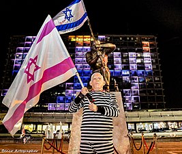 פסל גיבור ישראל בחזית בית עיריית תל אביב-יפו ולפניו מפגין מחופש לנתניהו במדי אסיר