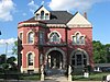 A brick house with windows of many sizes, a turret, and an arched entryway, surrounded by statues and a metal fence.