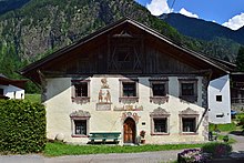 Bâtiment aux murs blancs et au toit en bois noir de style suisse avec montagnes en arrière-plan en été.