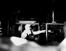 A person in an exposure suit and respirator points to a burnt-out glove box.