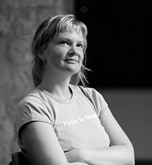 A black and white photograph of a blond woman looking up with arm cross about her "I Love To Share" shirt