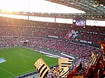 Photographie montrant la tribune d'un stade, avec un blason de grande taille en tissu, déployé par la foule.