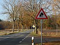 Straße mit durch Bäume ein­ge­schränk­tem Licht­raum­profil und ak­tu­el­lem Verkehrs­zei­chen