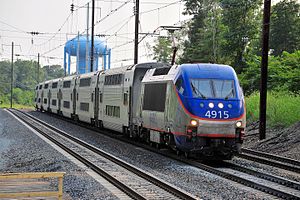 Blue and silver locomotive with orange striping pulling seven bilevel carriages on triple-track