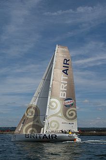 De profil, bateau blanc marchant sous voile non loin de la côte.