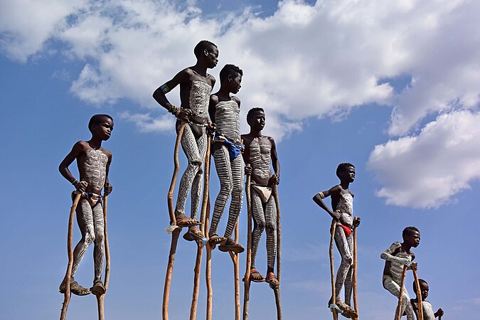 圖為埃塞俄比亞的班納族孩童，身上畫有傳統的彩繪，站在木製的高蹺上。