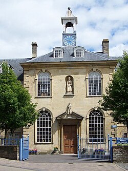 Yellow stone building with central 2 storey block with hipped roof and flanking 3 storey blocks