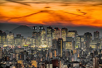 Aerial view of a city; many low-rise buildings in the foreground with many high-rise buildings in the background. The summit of a snow covered mountain can be seen in the distance.