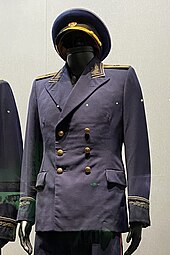 Un uniforme noir à boutons et galons dorés présenté sur un mannequin.