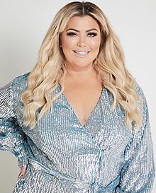 A blonde woman wearing a blue sparkly dress smiles towards the camera