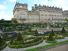 Au premier plan le vaste jardin à la française entourant un bassin ; derrière, la façade néoclassique en pierre blanche du château