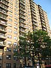 The front of 1520 Sedwick Avenue. A light brown apartment building is in the background with some trees in the foreground.