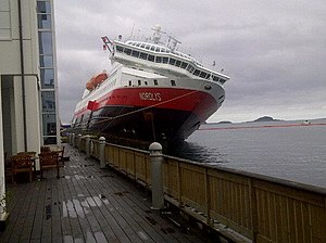 Photograph of a large boat whose starboard side is listing and riding up against the harbor