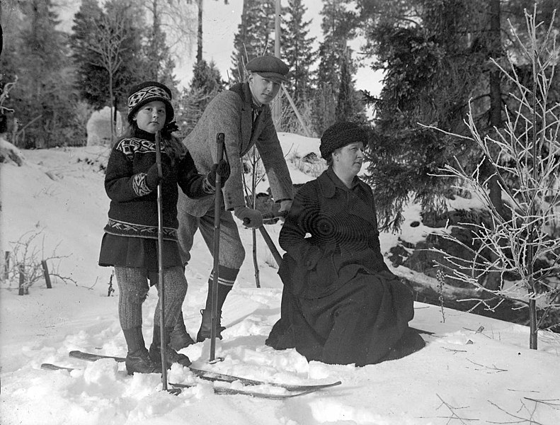 File:Vinterbild. Gruppfoto av en kvinna som sitter på en sparkstötting och en pojke och en flicka på skidor - Nordiska Museet - NMA.0057526.jpg