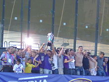 Multiple people celebrating at the podium with a trophy in their hands.