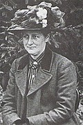 Photographie noir et blanc de Beatrix Potter portant un chapeau à fleurs.