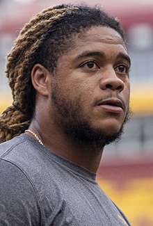 A close up photograph of a man with dreadlocks in a t-shirt