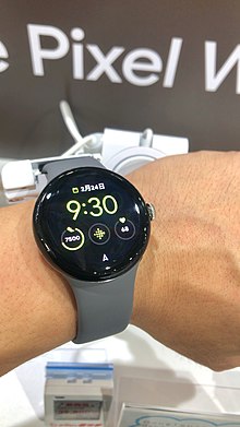 A Pixel Watch being worn on the left wrist. The screen indicates it is February 24 at 9:30, and is measuring heart rate (68 beats per minute) with a total step count of 7,500 for the day.