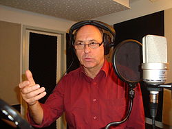 Uwe Karpa seated, speaking into a microphone while wearing headphones