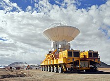 Large white parabolic-dish antenna on yellow, multi-wheeled vehicle