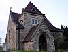 A squat stone church with a gabled porch, beyond which is a low tower with a pyramidal roof, and the body of the church is behind this