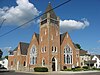 A red brick church with a prominent tower and stained-glass windows, sitting in front of a blue sky