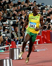 Usain Bolt in a yellow running vest and green shorts just completing a race