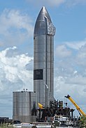 Photograph of a large, mostly featureless silver rocket at a facility