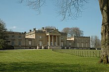 A mansion with two adjacent wings, with a gravel drive and lawn in front