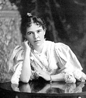 Photo of Blanche Blick Burnham taken in 1896 in Bulawayo, Rhodesia. She is seated at a table and her head is leaning on her right arm. She is wearing a flowing dress.