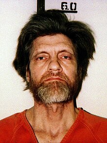 In orange prison garb, an unshaven Kaczynski stares sternly at the camera.