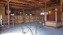 A building interior with a pair of tram tracks leading to individual gates and a small horse stable on the right