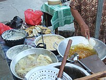 Verschieden große Kochgefäße und Schüsseln sind gesehen. Eine Person rührt in einer Schüssel. In jedem Gefäß ist eine andere Zutat zu erkennen.