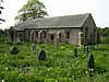 A long low simple stone church seen from the southeast with a south porch and a west bellcote