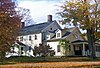 A light yellow house lit by sun from the left with trees in autumn color