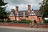 Photograph of a red-brick gabled building with black-and-white timbering to the gables and two large chimneys