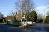 Street scene with area between two roads containing trees and stone column behind a white fence.