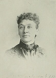 B&W portrait photo of a middle-aged woman with her hair in an up-do, wearing a dark high-collared blouse.