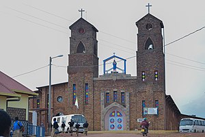 Frontalansicht eines Kirchengebäudes aus Backstein, das zwei Kirchtürme aufweist. Auf der Straße vor der Kirche ist eine Gruppe Jungen in Schuluniform unterwegs.