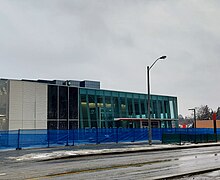 Photo of a largely completed underground light rail station in glass and white panelling with orange accents.