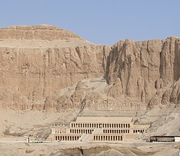 A massive limestone temple towered over by cliffs of great height