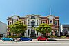 Façade of a heritage building behind two trees and in front of a blue sky