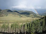 A small river winds through mountains under a rainbow.