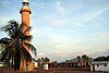 Cape Don Light, a tall, cement coloured lighthouse, with palm trees in front of it and a keeper's house to the right