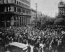 Large group of people in the middle of a city street beside a large concrete building