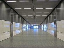 Long and wide pedestrian tunnel with grey tiled floor and white reflective walls